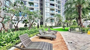 A courtyard with lounge chairs, greenery, and a tall building in the background. - Sophia Housing - Vinhomes Sky Lake Pham Hung (Hanoi)