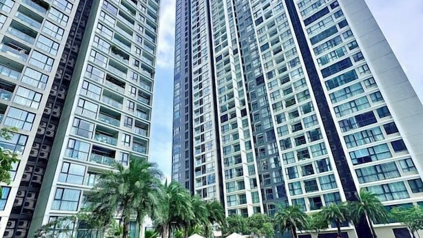 A high-rise residential building with multiple balconies, a swimming pool, and palm trees. - Sophia Housing - Vinhomes Sky Lake Pham Hung (Hanoi)