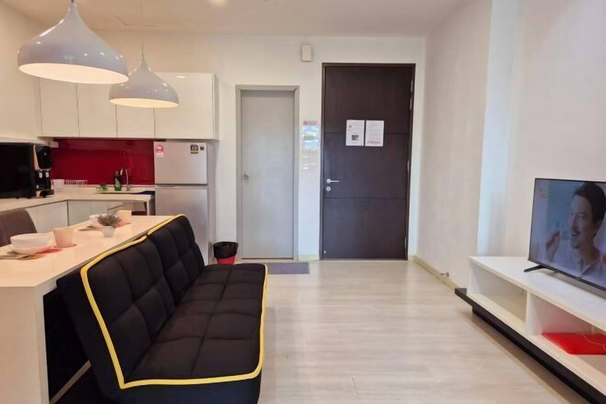 Ett modernt vardagsrum med en svart soffa, en matplats med ett vitt bord och ett kök med vita skåp och en röd väggbeklädnad bakom diskbänken.