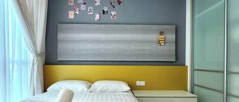 A hotel room with a bed, a headboard, a bedside table, and a window with curtains.