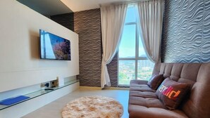 Een moderne woonkamer met een flatscreen televisie, een rond tapijt, een bruine bank met een kleurrijk kussen en een stadszicht door het raam.