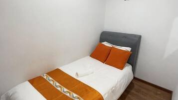 A single bed with a grey headboard, white bedding, and an orange throw blanket.