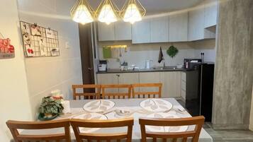 A dining area with a table set for four, wooden chairs, and a kitchen in the background.