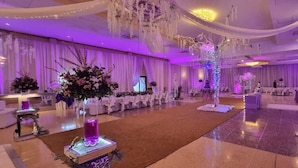 Un amplio salón de banquetes con largas mesas, cortinas decorativas y centros de mesa florales.