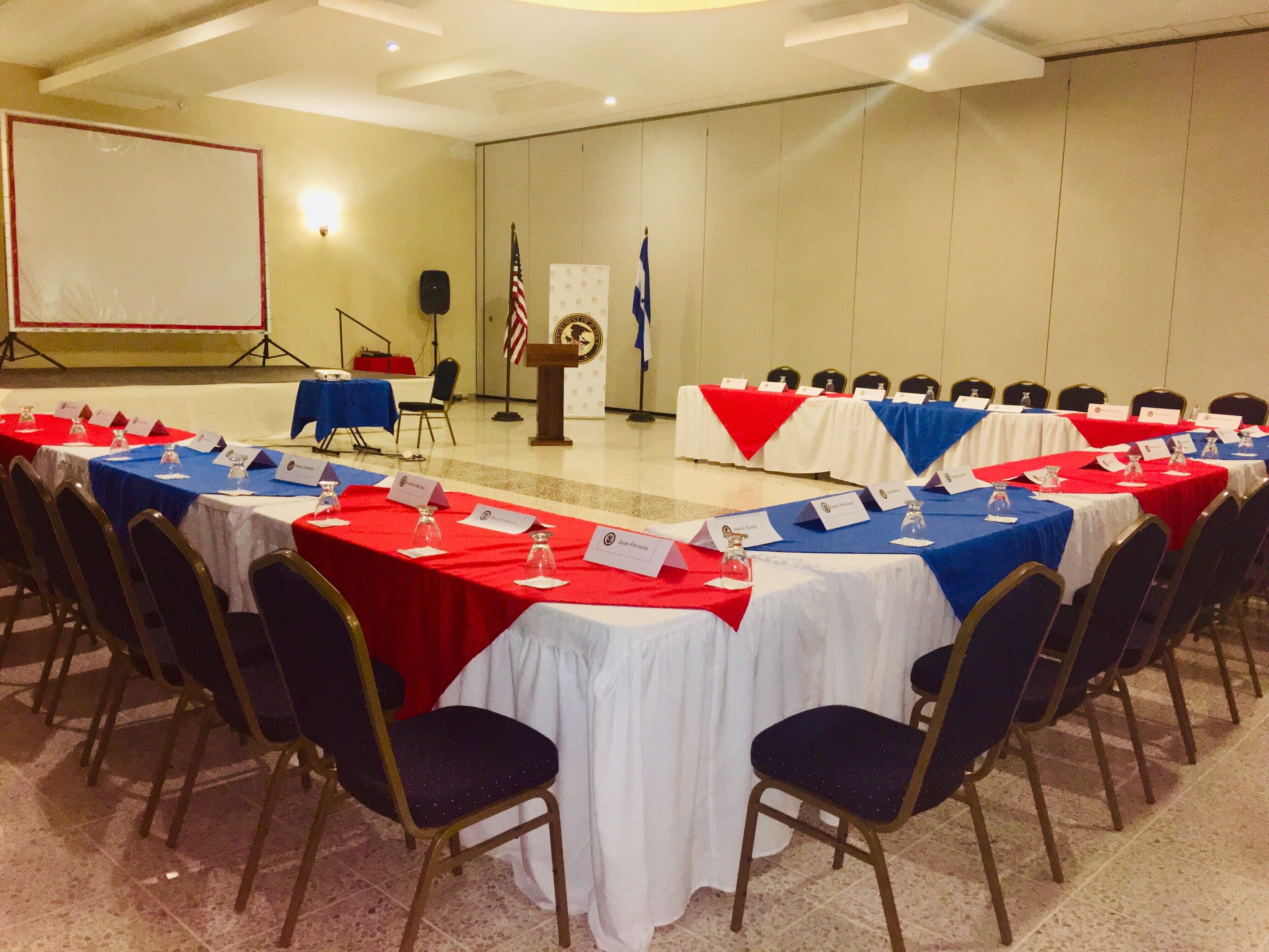 Un salón de conferencias con varias mesas, sillas y un atril con banderas.