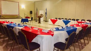 Un salón de conferencias con varias mesas, sillas y un atril con banderas.