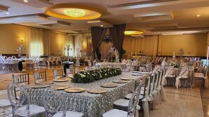 Un salón de banquetes con mesas redondas, sillas transparentes y un largo centro de mesa floral.