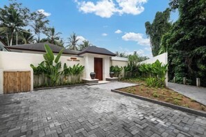 A modern house with a paved driveway, a wooden gate, and tropical plants. - Villa Arcadia by BaliSuperHost (Bali)