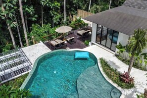 A swimming pool with a curved edge, surrounded by lounge chairs and umbrellas, and a view of a modern building with large windows. - Villa Arcadia by BaliSuperHost (Bali)