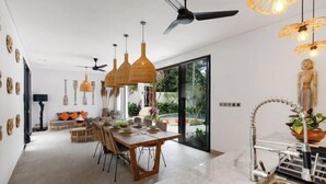 A modern dining area with a table set for four, a ceiling fan, and a view of the outdoors. - Villa Arcadia by BaliSuperHost (Bali)