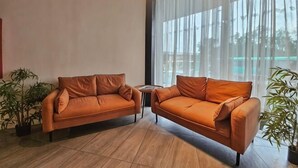 A modern living room with two orange sofas, a small table, and potted plants. - Terra Hotel Kawit (Kawit)