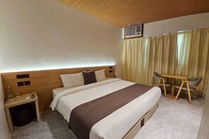 A hotel room with a bed, bedside table, and a small desk with a chair. - Terra Hotel Kawit (Kawit)