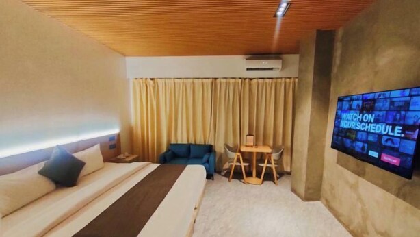 A hotel room with a bed, a TV mounted on the wall, a small table, and a blue chair. - Terra Hotel Kawit (Kawit)
