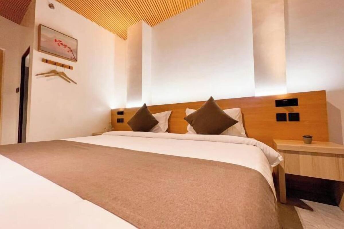 A modern hotel room with a large bed, wooden headboard, and a bedside table with a lamp.