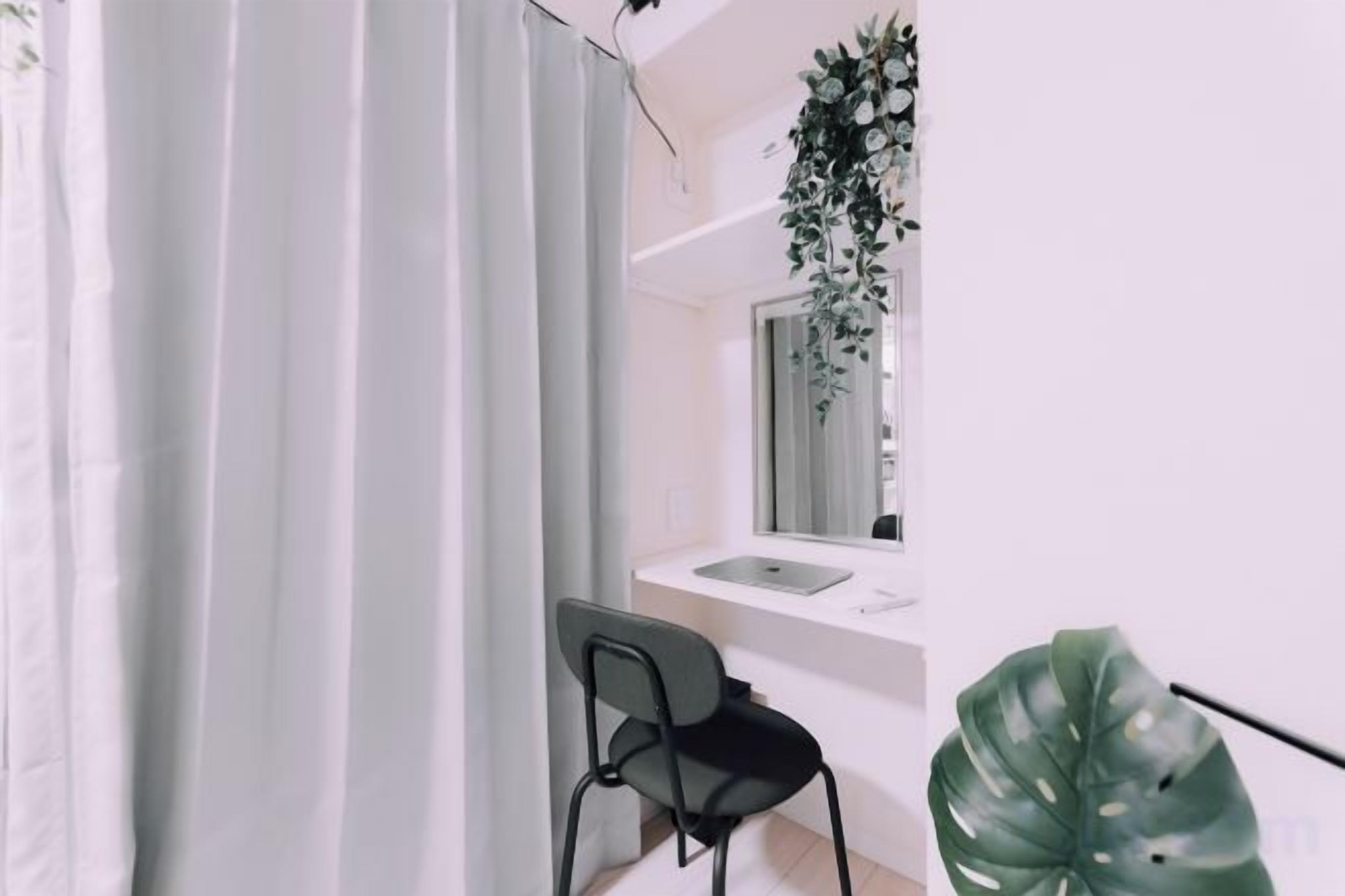 A bathroom with a white sink, a mirror, a black chair, and a large green plant.