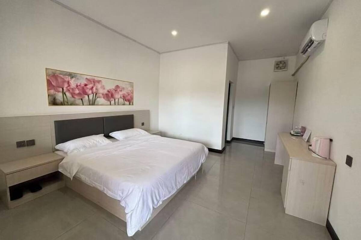 Ein modernes Hotelzimmer mit einem großen Bett, einem Nachttisch, einem kleinen Schreibtisch und einem Bild an der Wand.