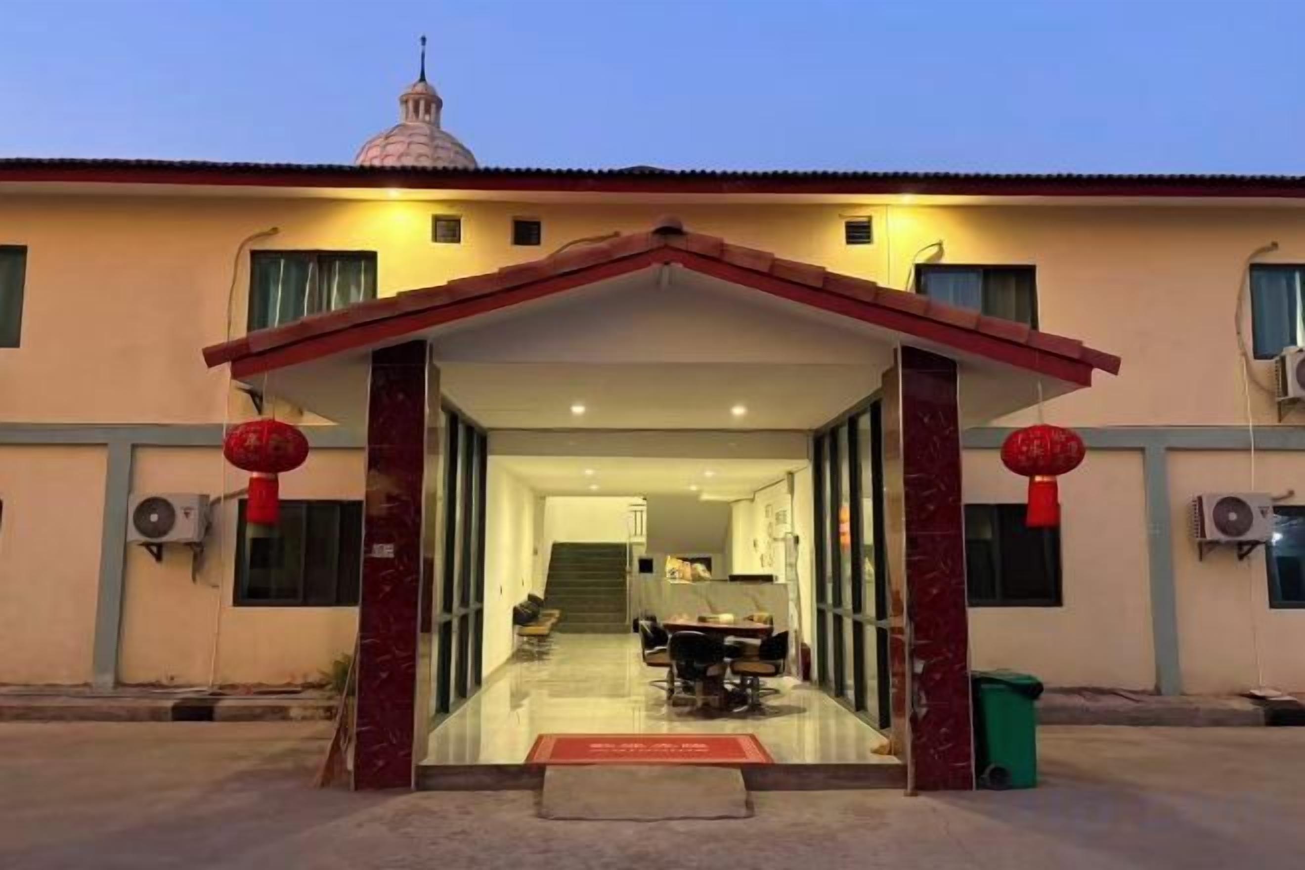 A building entrance with a covered walkway, a dining area inside, and a staircase leading to an upper level.