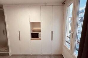 Una habitación con un armario grande, un estante pequeño con microondas y una ventana con vistas a edificios.