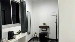 A compact room with a window, a small table with a plant, a black cabinet, and a white desk with a coffee maker. - White House (Ko Phi Phi)