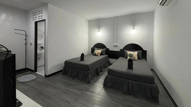 A small hotel room with two single beds, a desk, a chair, a TV, and an air conditioning unit. - White House (Ko Phi Phi)