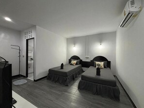 Ett litet hotellrum med två separata sängar, ett skrivbord, en stol, en TV och en luftkonditioneringsanläggning.