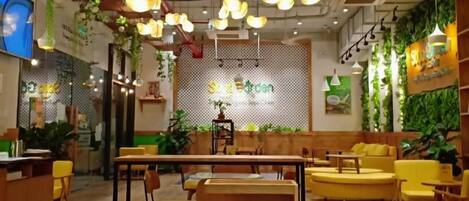 L’intérieur d’un restaurant, avec des tables, des chaises, des luminaires suspendus et un mur végétal.