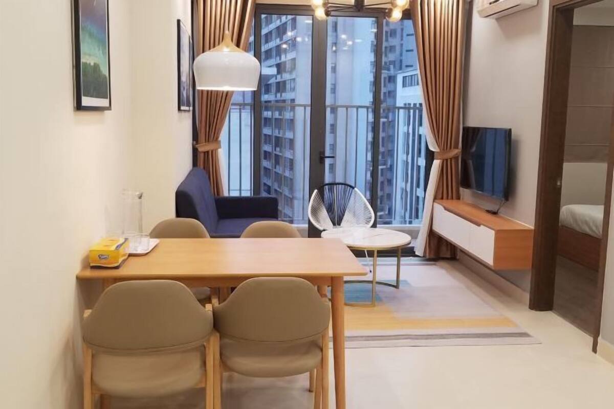 A modern living room with a dining table, chairs, a sofa, a TV, and a balcony with curtains.