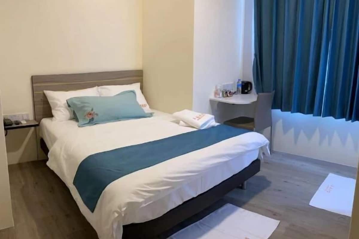 A neatly made bed with a blue and white bedspread, a bedside table with a lamp, and a window with curtains.