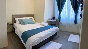 A hotel room with a bed, a nightstand, a small table with a lamp, and a window with curtains.