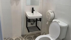 A bathroom with a white sink, black faucet, and a toilet with a paper towel dispenser.