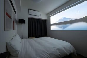 A hotel room with a bed, a window with a mountain view, an air conditioning unit, and a lamp. - Garden Otsuka (Tokyo)