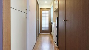 A narrow hallway with wooden flooring, a door at the end, and cabinets along the walls. - Garden Otsuka (Tokyo)