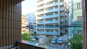A view from a window with a metal railing, overlooking a parking lot with several cars and a multi-story building in the background. - Garden Otsuka (Tokyo)