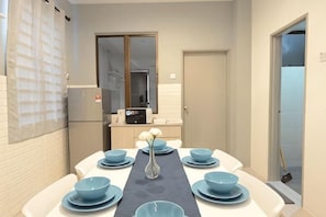 A dining area with a long table set with blue bowls and plates, a vase, and a small table with a computer.
