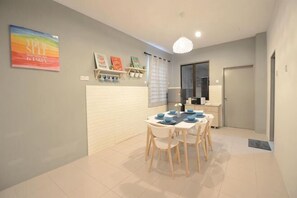 A dining area with a white table and chairs, a pendant light, and a door in the background. - De cozy Homestay (8-14 pax) (Ipoh)