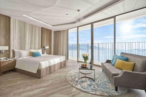Une chambre d’hôtel avec un grand lit, un canapé, une petite table avec un vase et une vue sur la mer.