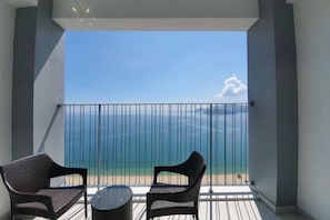 A balcony with two wicker chairs and a small round table, overlooking a beach with a clear sky.