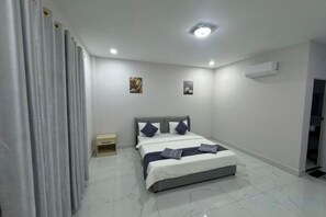A bedroom with a bed, a nightstand, a wall-mounted air conditioner, and a door. - Rosi Guesthouse & Coffee3 (Sihanoukville)