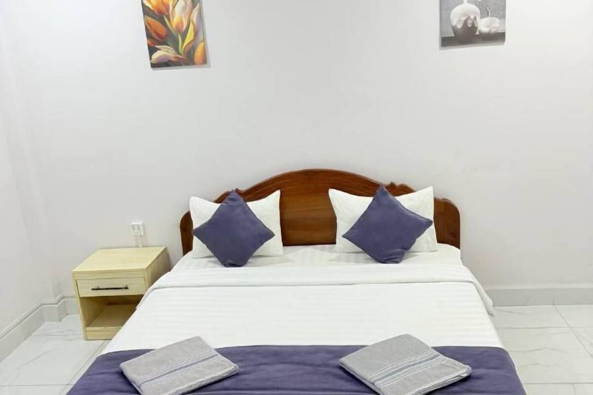 A neatly made bed with a wooden headboard, a bedside table, and two pillows.