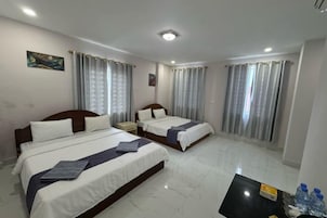 Quarto de hotel com duas camas, uma mesa de cabeceira, uma mesa com garrafas de água e cortinas.