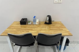 Una mesa de madera con dos sillas negras, una caja negra, una botella de agua, un vaso y una cafetera.