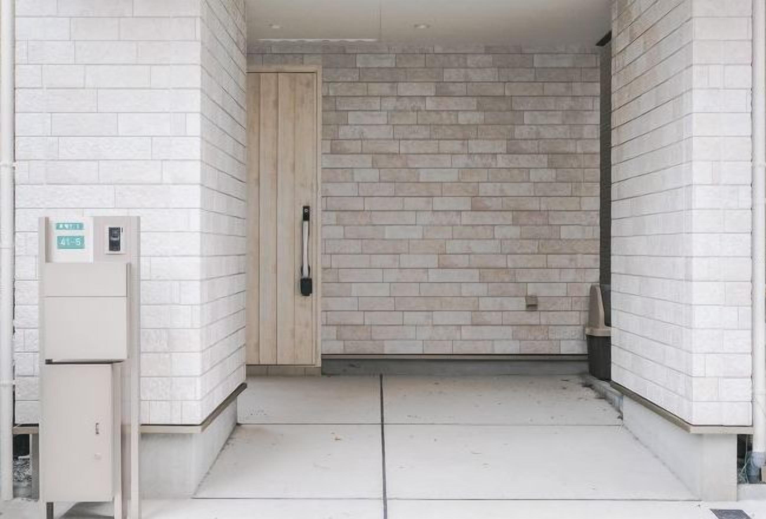 A hallway with white tiled walls and a wooden door. There is a small sign on the wall and a trash bin to the right.