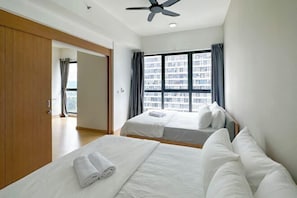 A hotel room with two beds, a ceiling fan, a large window with curtains, and a view of a cityscape.