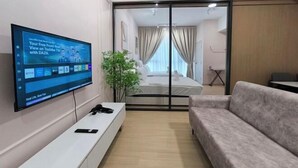 A modern hotel room with a flat-screen TV, a sofa, a bed with curtains, and a plant. - D'Sara Sentral Condo (Petaling Jaya)