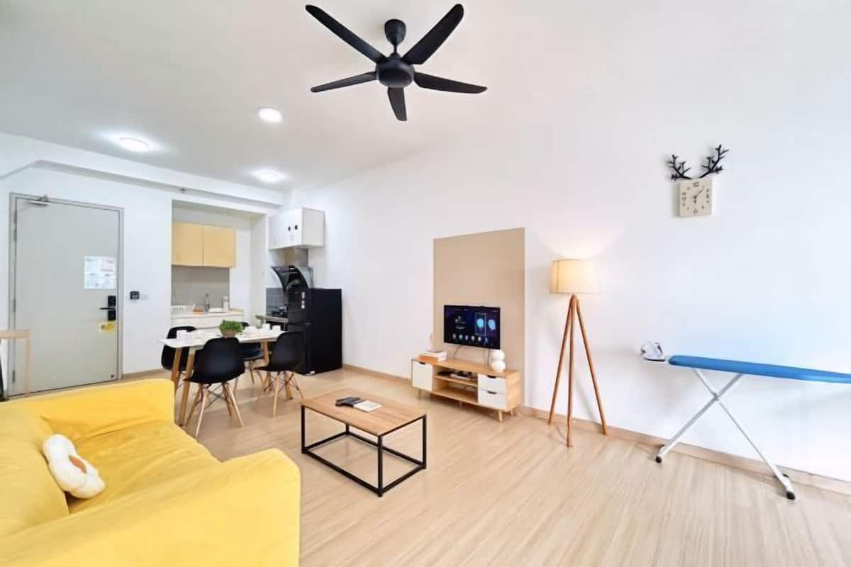 Un salon moderne avec un canapé jaune, une table basse, un téléviseur, un ventilateur de plafond et un coin repas comprenant des chaises et une table.
