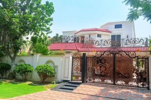 A gated entrance with a decorative gate, a red-tiled roof, and a well-maintained lawn.
