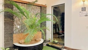 Un intérieur moderne agrémenté d’un mur décoratif, d’un bac circulaire contenant un palmier et d’une porte en verre donnant sur une autre pièce.