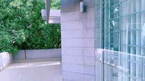 Un espace extérieur carrelé avec une porte en verre, un mur en béton et un arbre en arrière-plan.