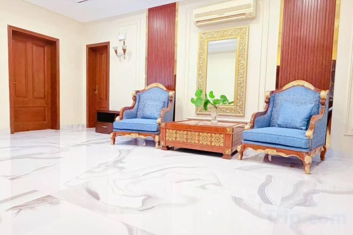 A room with two blue upholstered chairs, a wooden coffee table, and a large mirror with a decorative frame.