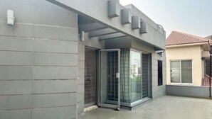 Un bâtiment moderne à la façade grise, doté de grandes portes coulissantes en verre et d’une terrasse carrelée.